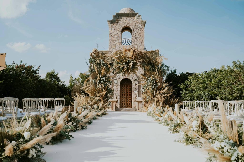 Beautiful outdoor wedding aisle with floral decorations leading to a stone building under a clear sky.