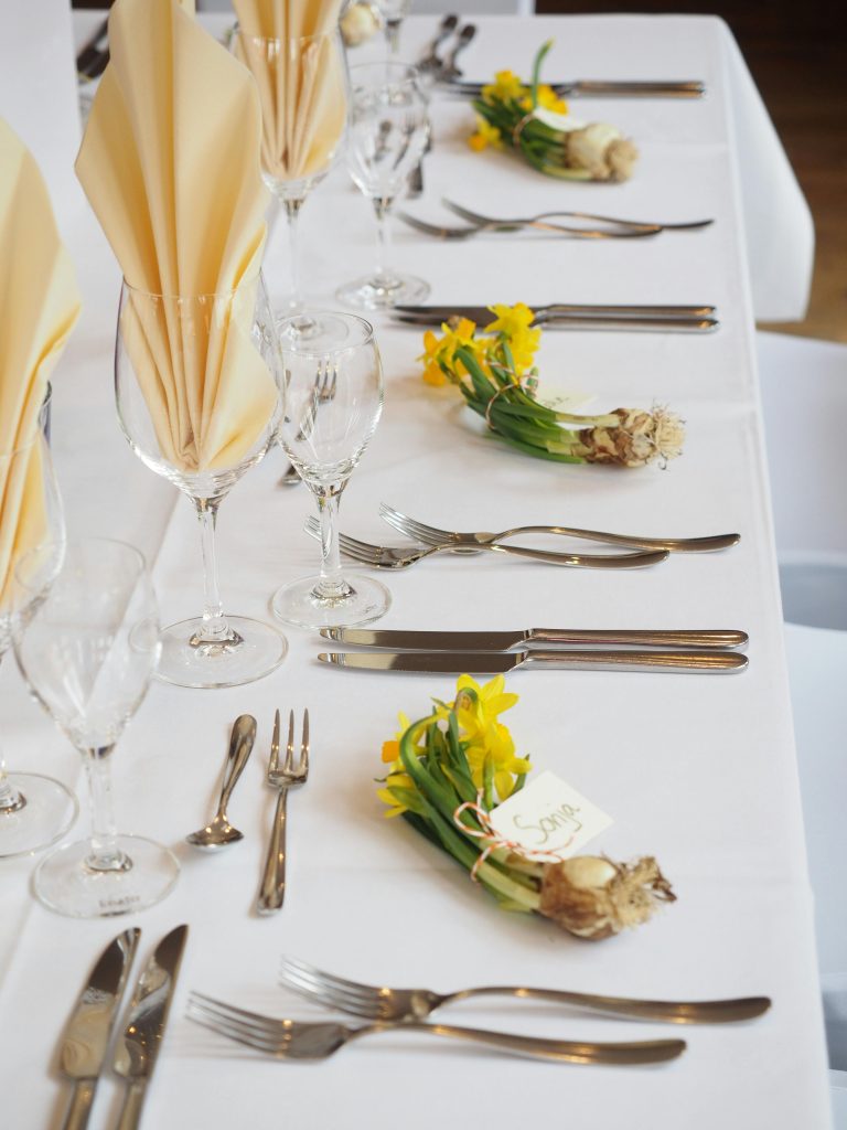 Sophisticated dining arrangement with daffodils and fine cutlery on a white tablecloth.